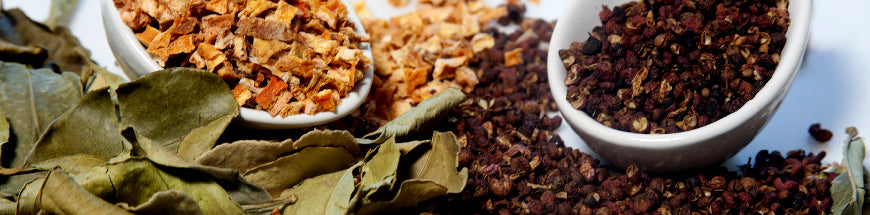 Dried bay leaves, crushed orange peels in a bowl, and whole dried Sichuan peppercorns in a bowl, all arranged closely together on a white background.