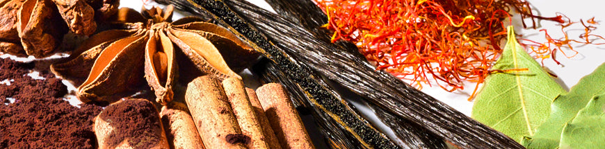 A close-up of various spices, including star anise, vanilla beans, cinnamon sticks, saffron threads, bay leaves, and ground spices arranged on a white background.