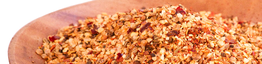 A wooden bowl filled with a colorful blend of crushed red pepper flakes and dried spices, set against a white background.