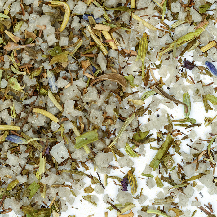 A close-up of Herbes de Provence Sea Salt by Whole Spice Inc. shows coarse French gray salt blended with rosemary, thyme, and purple flower petals, creating a vibrant seasoning mix displayed on a white background.