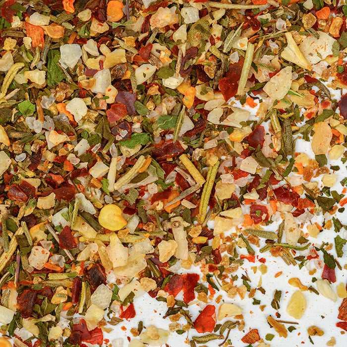 A close-up of Whole Spice Inc.'s Lamb Rub shows a colorful blend of dried herbs and spices, with vibrant red, green, and yellow piecesâlike onions, peppers, and Mediterranean seasoningsâscattered on a white surface.