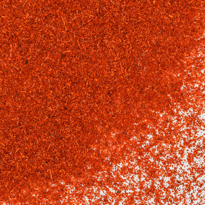 A close-up of Paprika Organic by Whole Spice Inc.—vivid red-orange organic spice—scattered across a white surface.