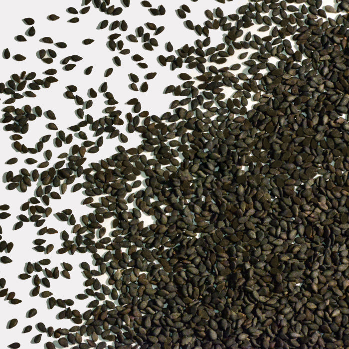 Whole Spice, Inc. Sesame Seeds Black Organic are scattered across a white surface, with most covering the lower half of the image and spreading upwards.