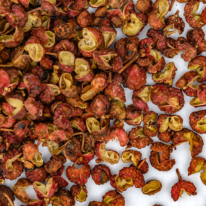 Close-up of Whole Spice Inc. Peppercorns Szechuan scattered on a white surface, displaying their reddish-brown color and wrinkled, hollow texture—a unique seasoning for poultry and various dishes.