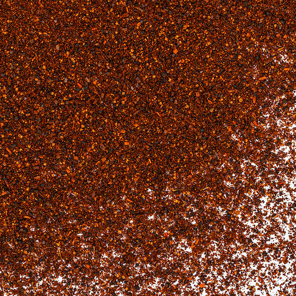 Whole Spice Inc. Dark Chili Powder, a bold spice blend, is sprinkled diagonally across a white surface—densest in the upper left and gradually lighter toward the lower right.