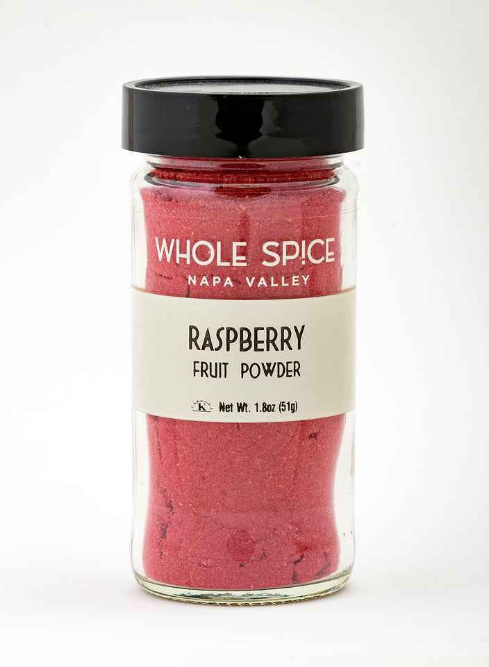 A glass jar from Whole Spice Inc. labeled Raspberry Fruit Powder contains vibrant pink-red powder. The jar features a black lid and a white label with a net weight of 1.8 oz (51g).