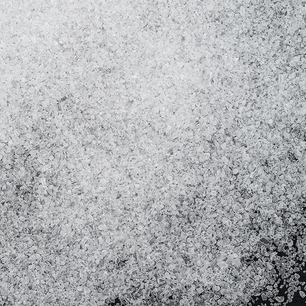 A close-up view of fine Sea Salt Fine crystals from Whole Spice Inc. scattered on a dark surface.