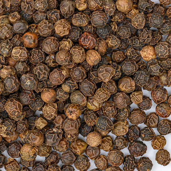 A close-up of Peppercorns Black Tellicherry by Whole Spice Inc. scattered on a white surface, highlighting their rough, wrinkled texture and rich dark brown color.