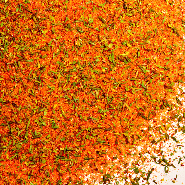 A close-up of Whole Spice Inc. Steak House Rub shows vibrant red, orange, and green flecks on a white background—an aromatic blend of herbs and powdered spices crafted for bold beef seasoning.