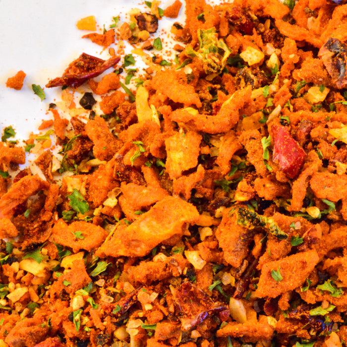 A close-up of Whole Spice Inc. Beans Seasoning—a vibrant, crunchy mix of dried fried onions, herbs, crushed red chili, and spices—scattered on a white surface.