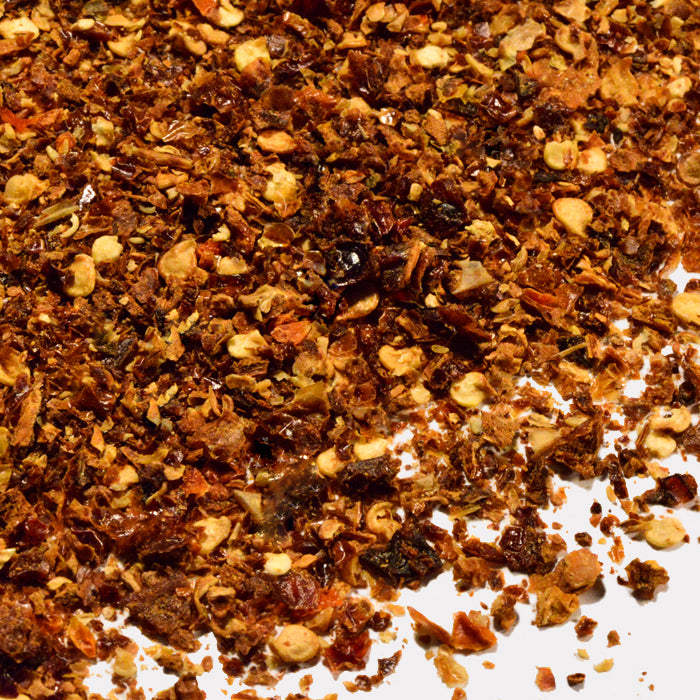 A close-up of Whole Spice Inc. Habanero Chili Crushed scattered on white, showcasing spicy dried habanero flakes and seeds—ideal for heat lovers seeking a bold boost in Scoville units.