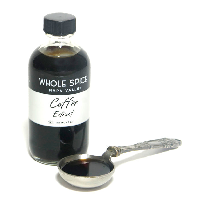 A bottle of Whole Spice Inc. Coffee Extract stands alongside a small silver spoon filled with the dark extract on a white background.