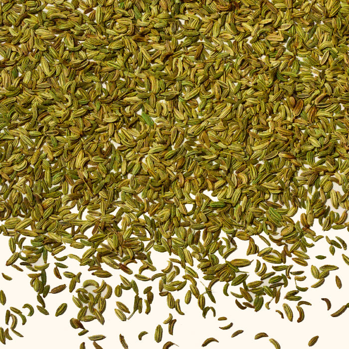 Close-up of Whole Spice Inc. Fennel Seeds Organic spread over a white surface—ideal for infusing aromatic flavor into your favorite spice blends and recipes.
