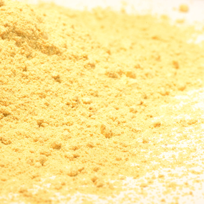 A close-up of Whole Spice Inc. Fenugreek Powder shows a loose pile of fine yellow powder spread on a white surface, commonly used in spice blends.