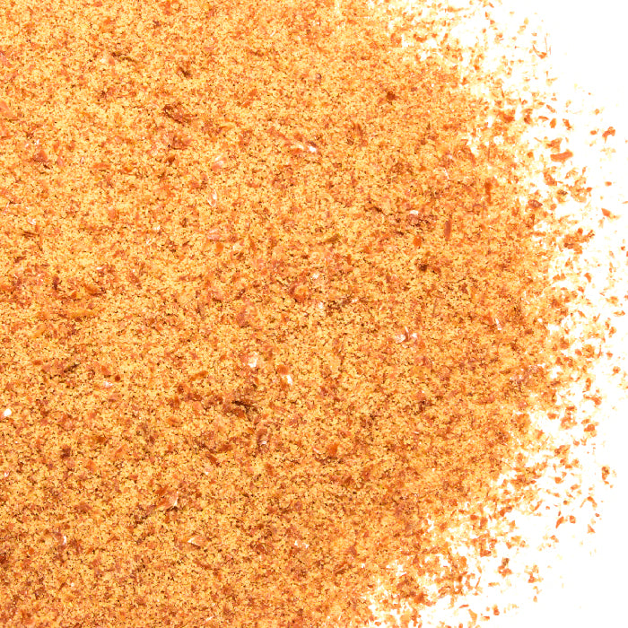 Close-up of Flax Seeds Ground by Whole Spice Inc.—orange-brown, fine granules—scattered across a white background, highlighting their heart-healthy antioxidant benefits.