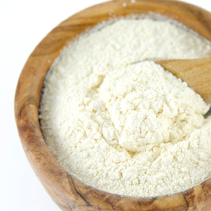 A wooden bowl holds fine, off-white Garlic Powder by Whole Spice Inc., with a wooden spoon resting inside.