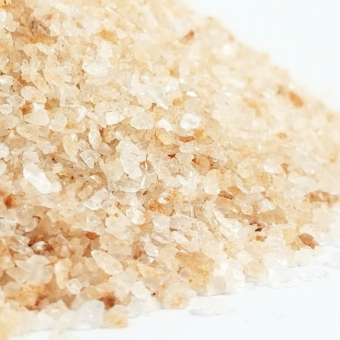 A close-up of Whole Spice Inc. Himalayan Pink Salt Fine #1 (0.2-0.8mm) crystals on a white surface, showcasing their fine texture, natural pink hues, and beneficial trace minerals.