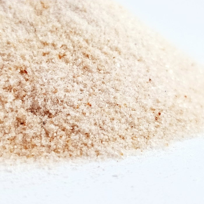 A close-up of fine, light brown Himalayan Pink Salt Powder (0.0-0.2mm) from Whole Spice Inc. on a white surface, highlighting its grainy texture and subtle color variations, rich in trace minerals.