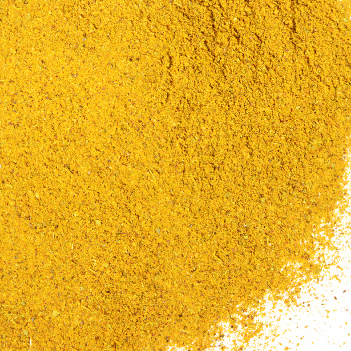 A close-up of Whole Spice Inc. Hot Curry Powder shows a dense pile of vibrant yellow spice on a white background, concentrated at the top left and scattered toward the bottom right.