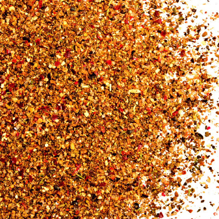 A close-up of Whole Spice Inc.’s Juniper Berry Spice Rub showcases its colorful blend of ground juniper berries, red pepper flakes, seeds, and herbs scattered on a white surface—ideal for seasoning game meat.