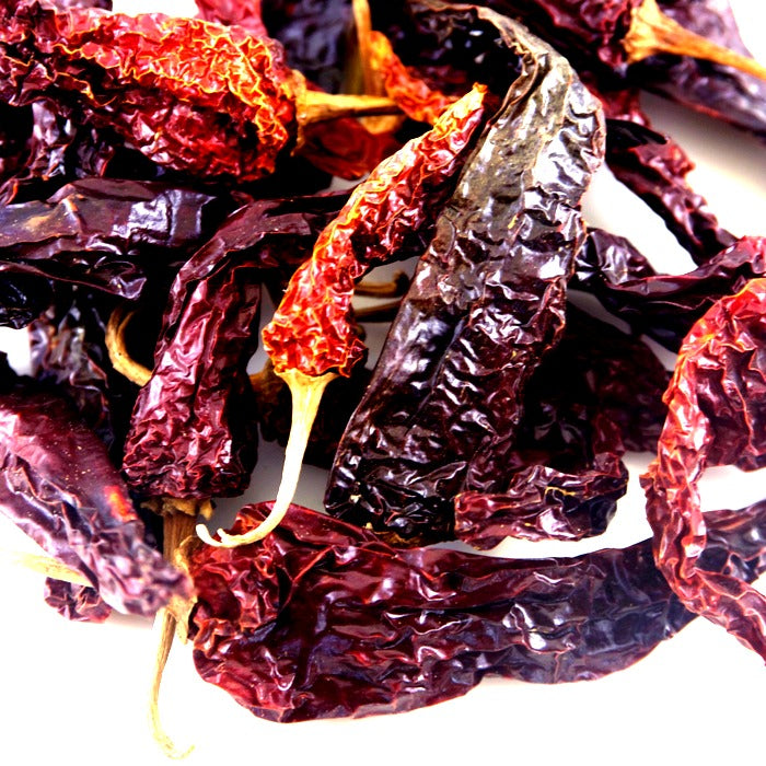 A pile of Kashmiri Chili Whole from Whole Spice Inc. displays vibrant red color and bold flavor, perfect for adding rich heat to your dishes.