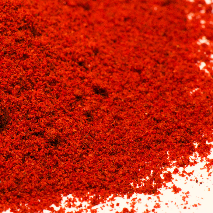 A close-up view of a pile of Bittersweet Smoked Paprika by Whole Spice Inc., finely ground and scattered on a white surface.