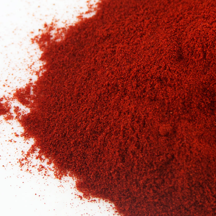 A close-up of finely ground Premium Spanish Paprika by Whole Spice Inc., featuring a vivid 120-140 Asta red color, scattered as a rich powder across a white background.