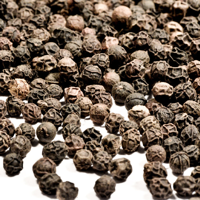 Close-up of Whole Spice Inc. Peppercorns Black Tellicherry scattered on a white surface, showcasing their prized quality.