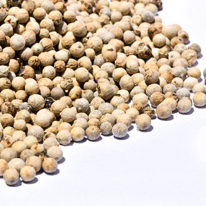 A close-up of Peppercorns White by Whole Spice Inc., ideal for white sauces, shows the dried peppercorns scattered on a white surface.
