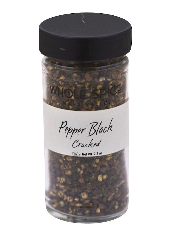 A clear glass jar with a black lid contains Pepper Black Cracked seasoning. The white label displays "Pepper Black Cracked," net weight 2.2 oz, and features the Whole Spice Inc. brand above the product name.