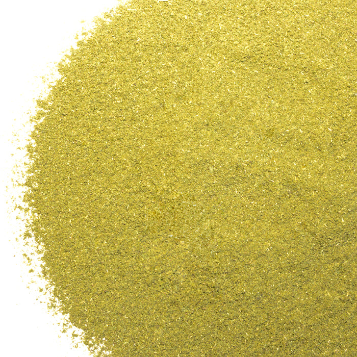 A close-up of Whole Spice Inc. Peppermint Powder shows fine, yellowish-green granules evenly spread on a white surface, highlighting its smooth texture.