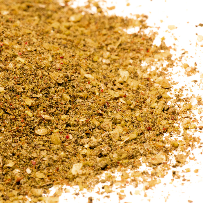 A close-up of Whole Spice Inc. Pesto Seasoning with a coarse texture in brown, yellow, and red hues on a white backdrop—ideal for adding bold flavor to Italian pasta or pesto tortellini dishes.