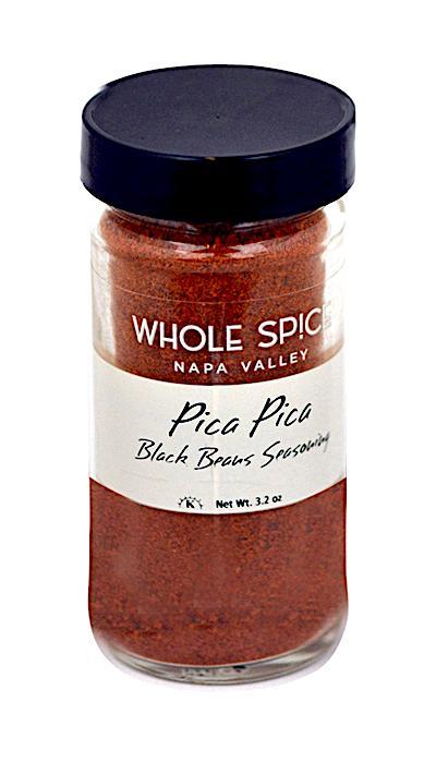 A clear glass jar with a black lid contains Whole Spice Inc. Pica Pica Black Beans Seasoning, a spicy reddish-brown chili blend perfect for adding kick to black bean salads. Net weight: 3.2 oz.