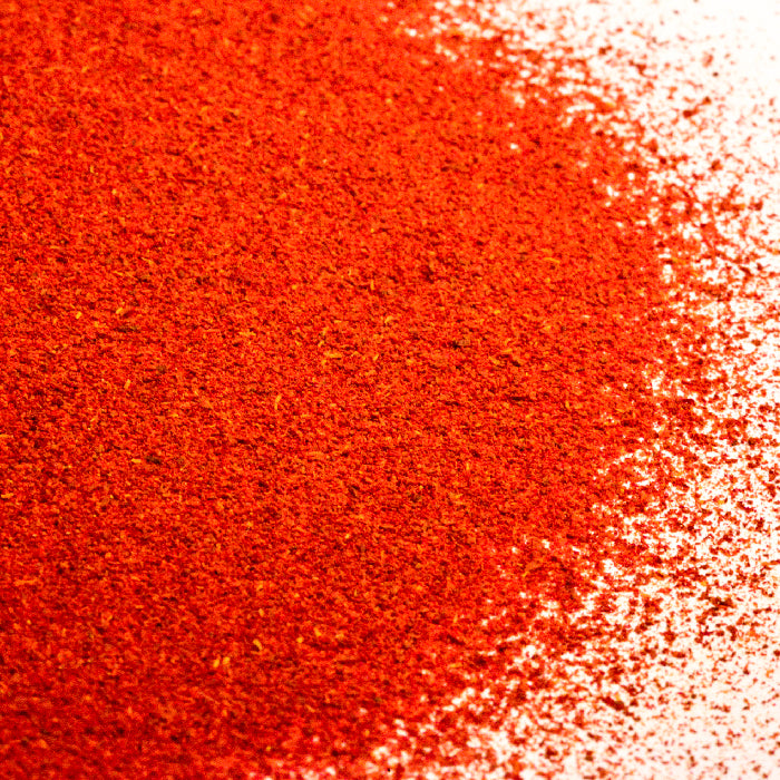 A close-up of Saffron Powder by Whole Spice Inc. shows a pile of finely ground red-orange spice scattered on a white surface.
