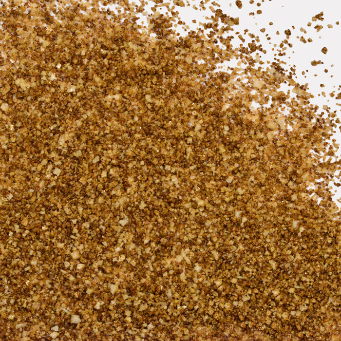 A close-up of scattered Porcini Mushroom Sea Salt granules by Whole Spice Inc. on a white surface, highlighting the salt’s texture and the uneven distribution of crystals.