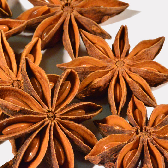 Close-up of Whole Spice Inc. Star Anise, showing star-shaped pods and glossy brown seeds on a light background—a key ingredient in pho and five-spice powder.
