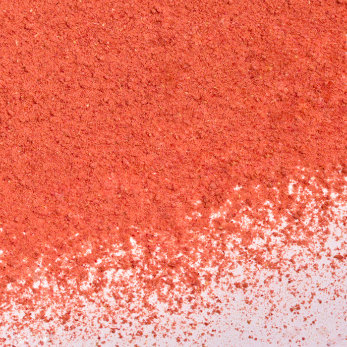 A close-up of Whole Spice Inc. Strawberry Fruit Powder, showing a vibrant, fine reddish-orange pile on a white surface that highlights the natural color and energy of dehydrated strawberries.
