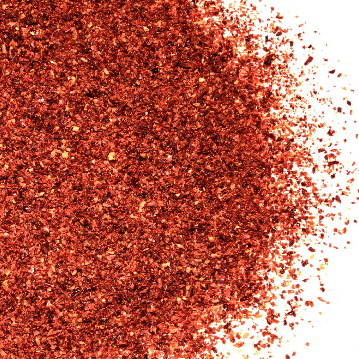 A close-up of Sun Dried Tomatoes Granulated by Whole Spice Inc. scattered on a white background, highlighting their rich texture and deep color—ideal for boosting flavor in pasta or sprinkling over fresh salads.