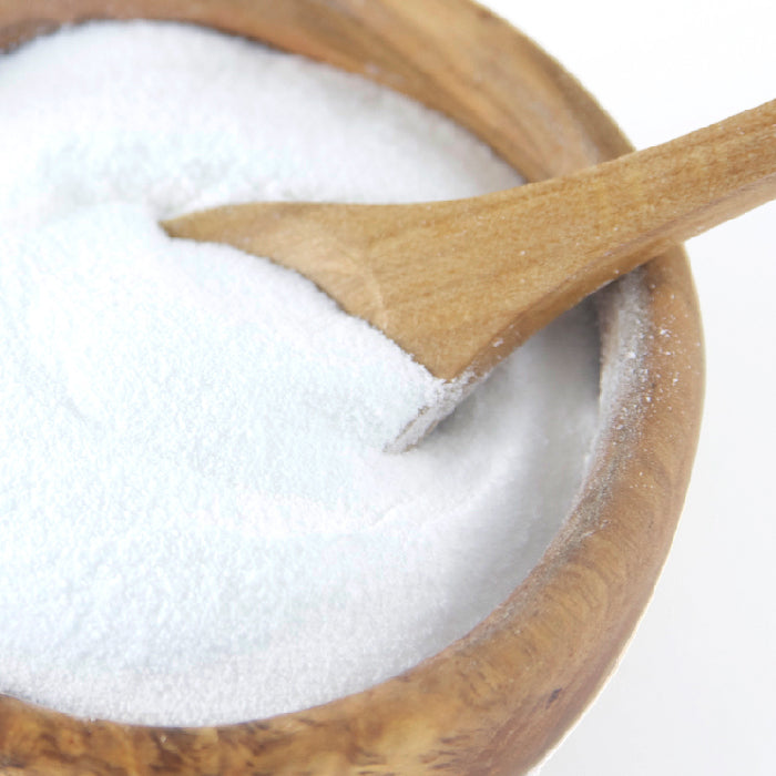 A wooden bowl holds Whole Spice Inc. Vinegar Powder, a fine white seasoning, with a small spoon inside scooping some of this unique ingredient.