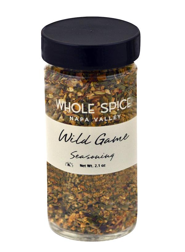 A clear spice jar from Whole Spice Inc., labeled Wild Game Seasoning, holds a 2.1 oz blend of dried herbs and spices with a black lid—ideal for poultry or lamb.