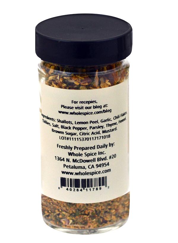 A clear spice jar with a black lid contains Wild Game Seasoning. The label from Whole Spice Inc. lists ingredients, contact info, their address and website, plus a barcode at the bottom.