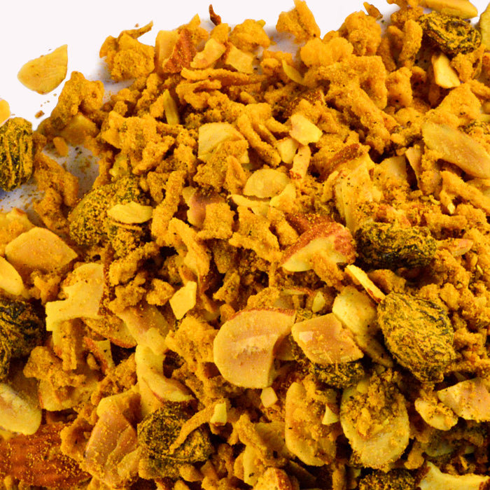 A close-up of a crunchy snack mix featuring Whole Spice Inc. Yemenite Rice Seasoning, roasted peanuts, and dried raisins scattered on a white surface.