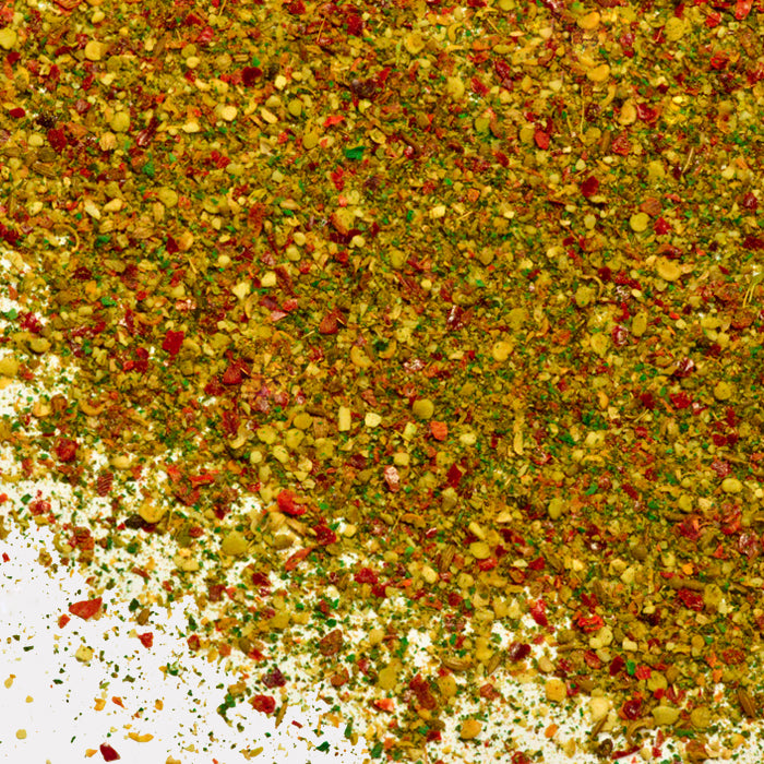 Vibrant Zhug Spice by Whole Spice Inc.âa colorful blend of red, green, and yellow bits, with dried herbs and crushed peppers scattered on a white surface.