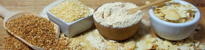 Various types of ground and sliced almonds in wooden and ceramic bowls and spoons are arranged on a wooden surface.