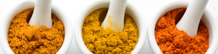 Three white mortar and pestles filled with orange, yellow, and red spices are lined up side by side against a white background.