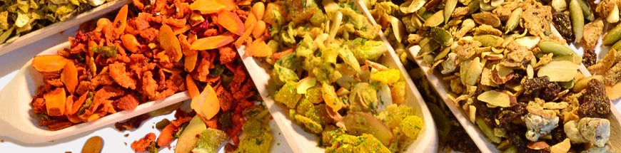 Close-up of three trays filled with assorted dried fruits, nuts, seeds, and colorful snack mixes, arranged side by side.