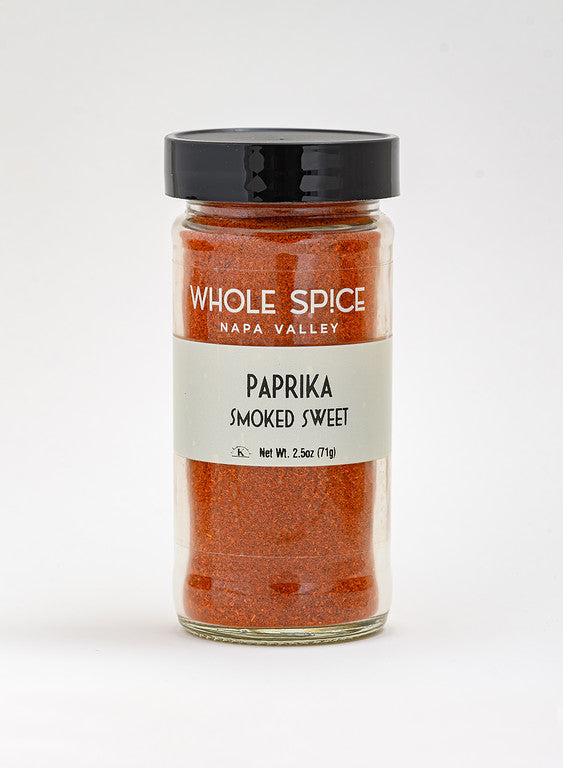 A clear glass jar with black lid contains Whole Spice Inc. Sweet Smoked Paprika, Net Wt. 2.5oz (71g). Ideal for adding rich Spanish paprika flavor to your dishes.