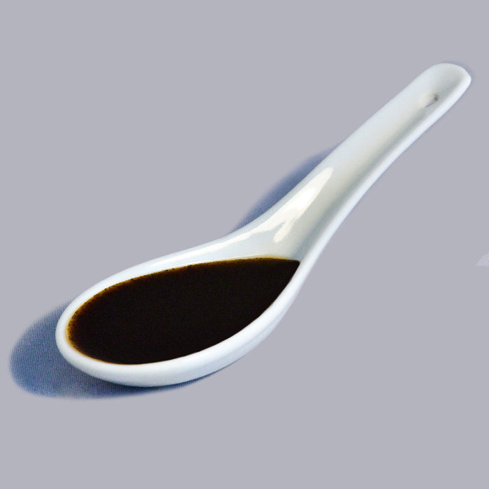 A white ceramic spoon filled with Whole Spice Inc. Vanilla Paste is placed on a light gray background.