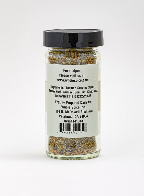 A glass jar of Whole Spice Inc. Za'atar Spice Blend with a black lid is shown from the back, labeling ingredients such as toasted sesame seeds, Za’atar herb, sumac, and sea salt—ideal for authentic Middle Eastern flavor.