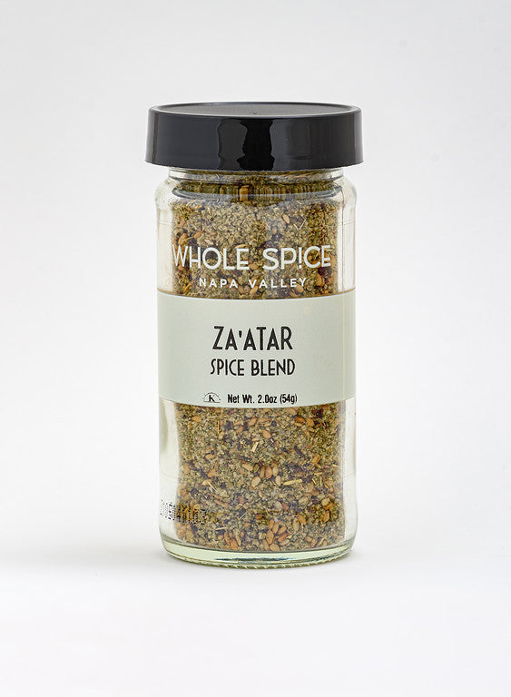 A clear glass jar with a black lid contains Za'atar Spice Blend by Whole Spice Inc. The label shows the product name, net weight of 2.0 oz (54g), and features this authentic Middle Eastern seasoning.
